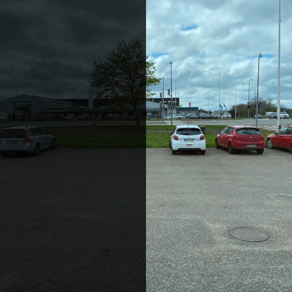 Venstre side er mørk, højre side viser klart parkeringsplads med biler og skyet himmel.
