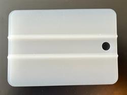 Rektangulær skraber med afrundede hjørner, to vandrette riller og et lille hul nær kanten.