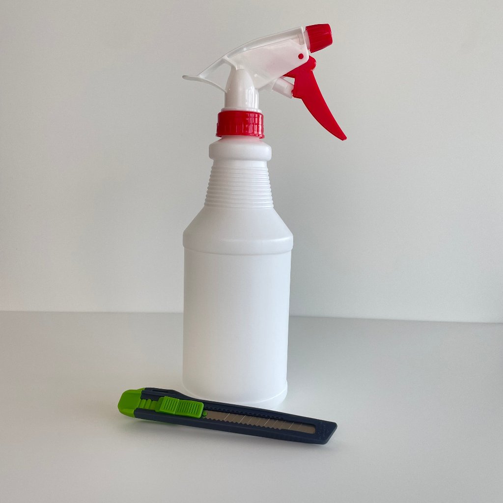 Hvid sprayflaske med rød dyse og sort-grøn hobbykniv med udtrækkeligt blad på lys baggrund.