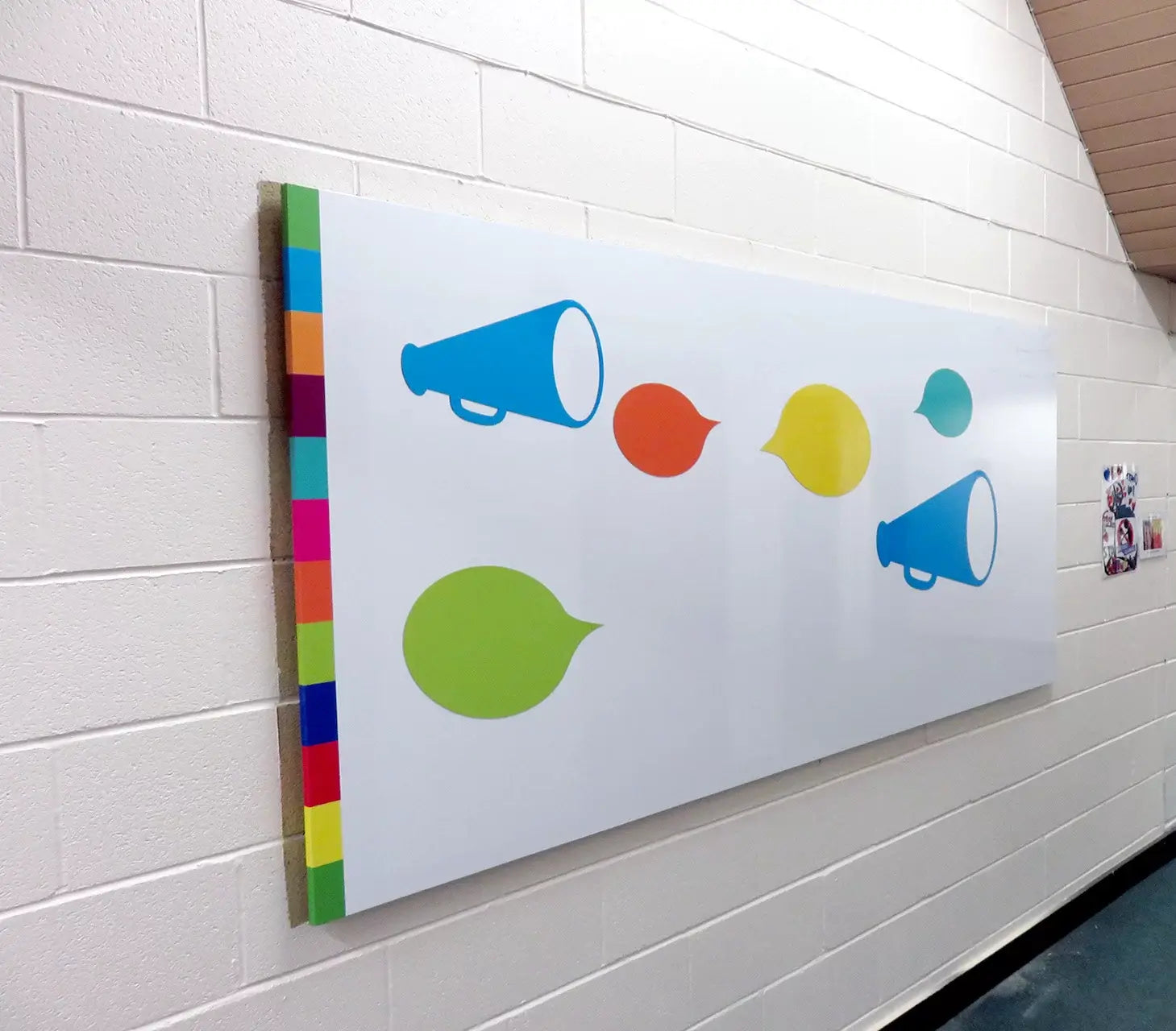 Whiteboard folie med farverige megafoner, talebobler og kvadratisk kantmønster på en væg.