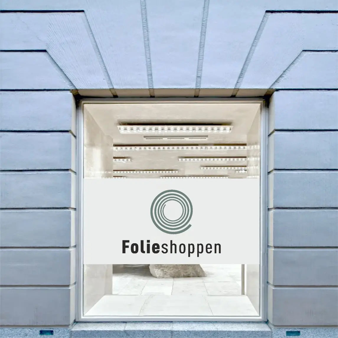 Vindue med sandblæst folie, logo og teksten "Folieshoppen" i en kommerciel bygning.