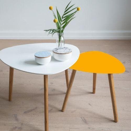 Lille bord med gylden overflade ved siden af hvidt bord med træben, vase og skål på det hvide bord.