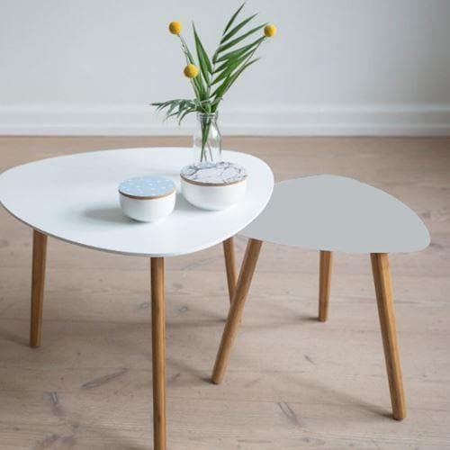 To små borde med træben, det ene med grå top, på et lyst gulv med dekorationer.