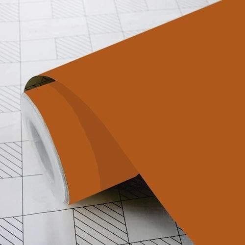 Rulle af mat, nøddebrun folie, delvist udrullet på skæremåtte med gittermønster.