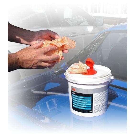 Hænder bruger 3M Håndrenseservietter fra beholder på biloverflade til rengøring.