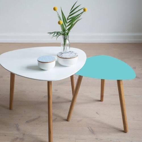 To små borde, et med pastel folie og et hvidt. Træben, vase med blomster og skål på det hvide bord.