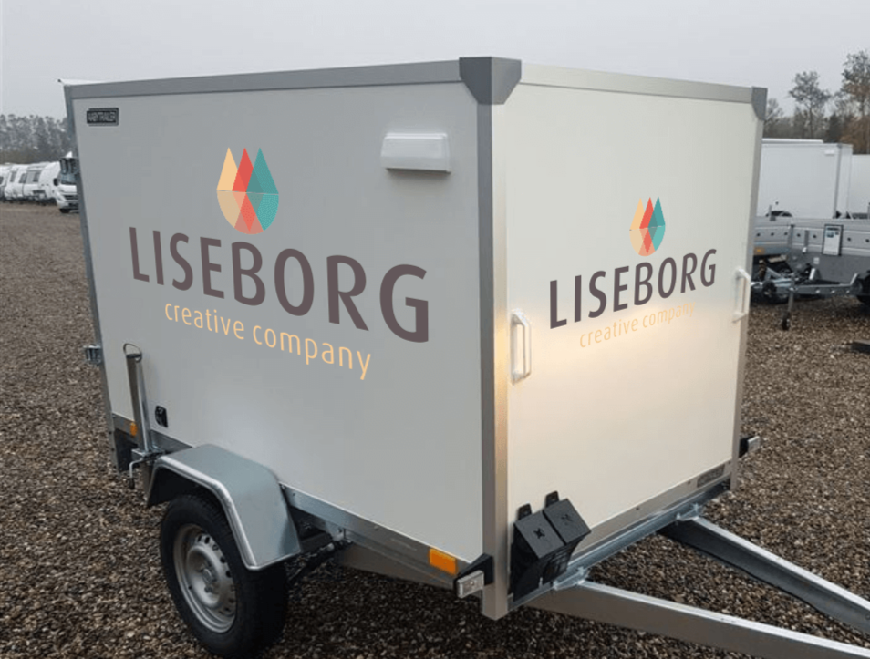 Trailer med grafisk design og logo på siden, står på grus med andre trailere i baggrunden.