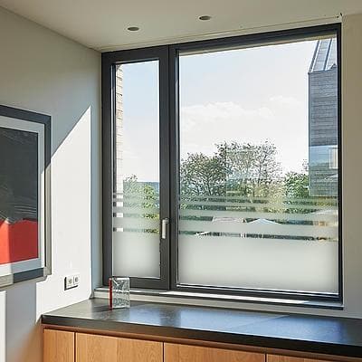 Moderne vindue med sandblæst film og vandrette striber i bunden, placeret i et lyst rum.