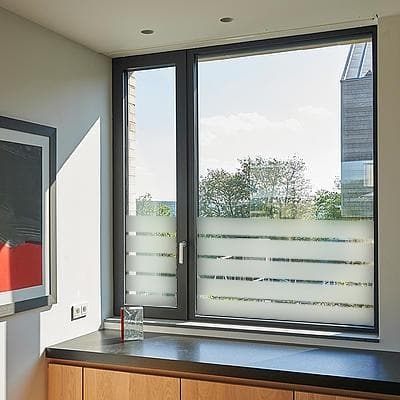 Vindue med frostet film i vandrette striber, giver privatliv og lysindfald, på glasoverfladen.