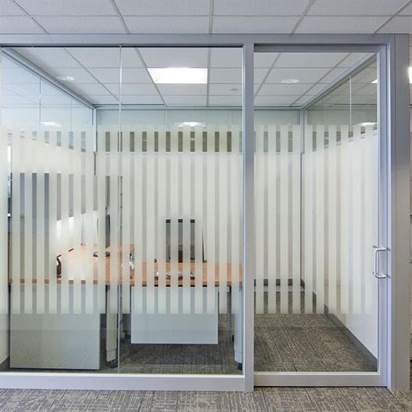 Kontormiljø med glasvæg og lodrette striber i frostet folie, der giver delvis privatliv.