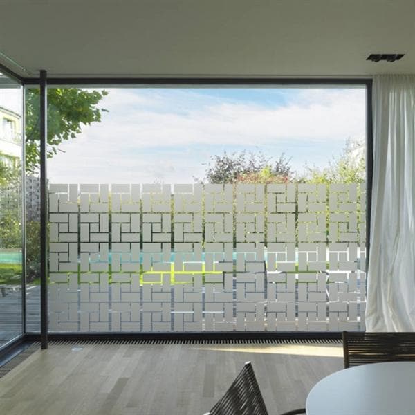 Stort vindue med geometrisk frostet film, der lader lys ind og giver privatliv i et lyst rum.